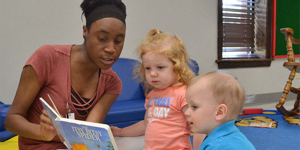 Student-worker in child study center reading a book to toddlers.