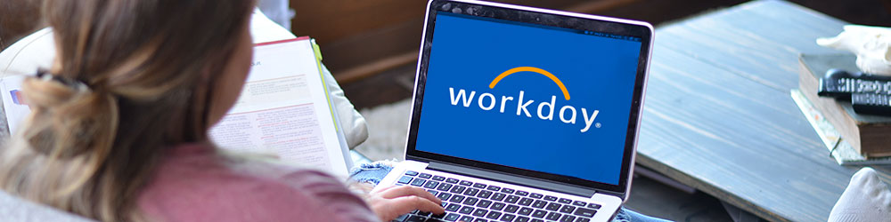 Over-the-shoulder shot of a student sitting at home working on a laptop with the Workday logo on a blue background on screen.